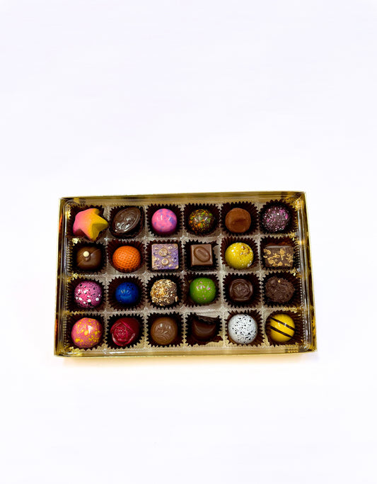 Boîte ouverte de 24 chocolats fins Rose Élisabeth, disposés dans un plateau doré, présentant des pièces colorées et artistiques aux motifs variés.