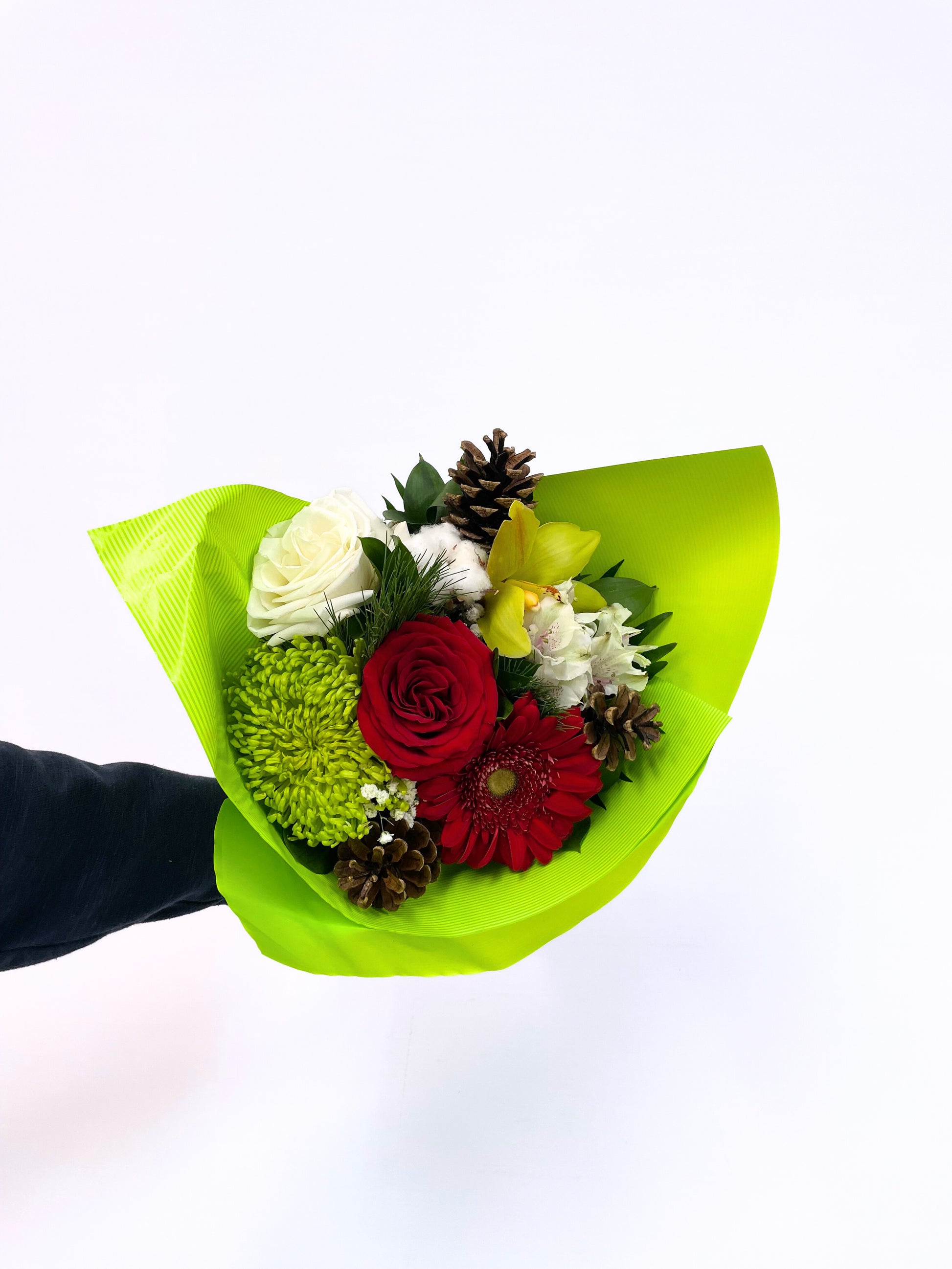 Bouquet festif “Esprit de Noël” avec roses rouges et blanches, gerberas rouges, orchidées jaunes, chrysanthèmes verts, pommes de pin et feuillages décoratifs.